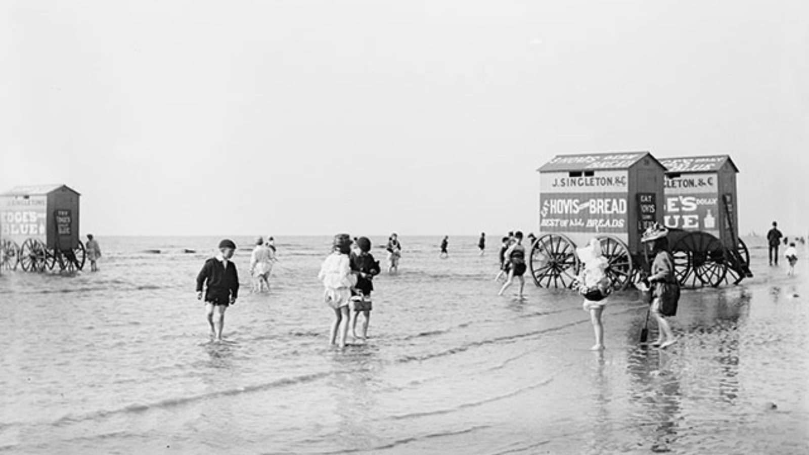 Children and bathing machines on the beach, with advertisements for 'J. Singleton & Co' and 'Hovis Bread: the best of all breads.'