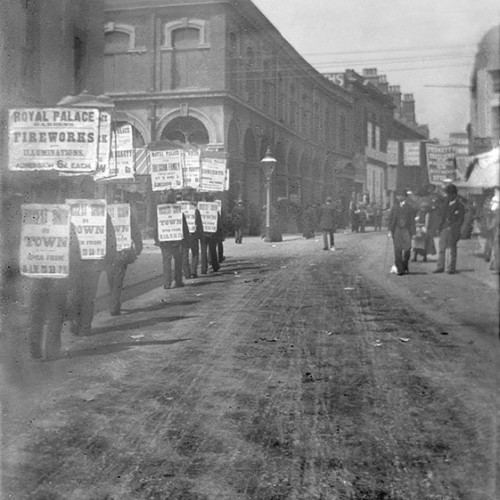 Men carrying advertising signs in street reading 'Royal Palace Gardens- Fireworks, Illuminations.'