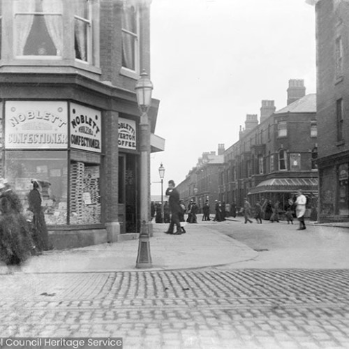 Street scene with people outside shop window with signs reading 'Noblett Confectioners.'