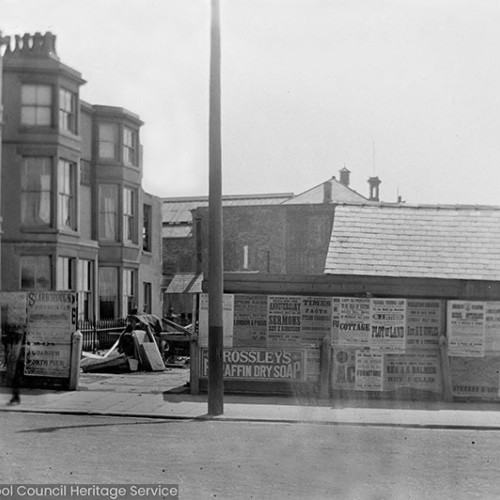 Street scene with advertising hoardings including adverts or 'Rossley's Paraffin Dry Soap' and 'Rev S.J. Balmer and Rev J. Ellis, Sermons.'