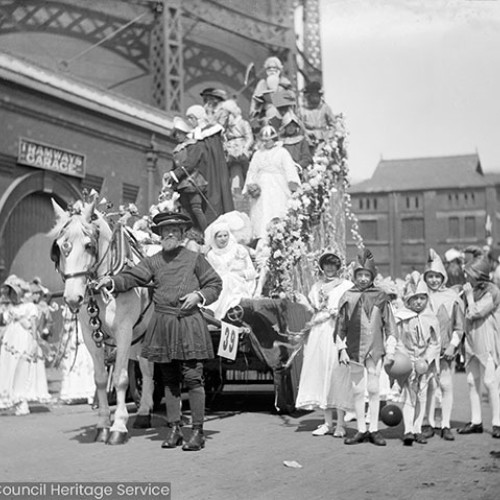 People in costume on carnival float, outside building with sign for 'Tramway garage.'