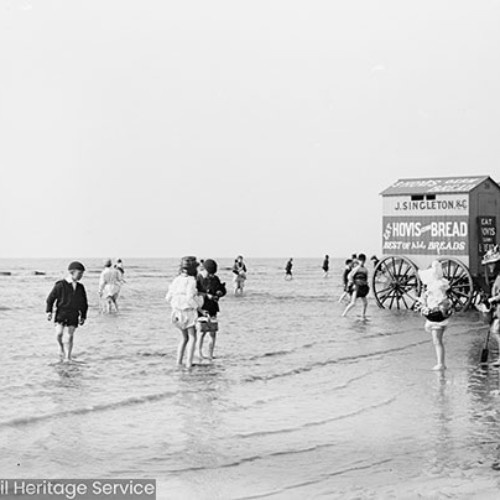 Children and bathing machines on the beach, with advertisements for 'J. Singleton & Co' and 'Hovis Bread: the best of all breads.'