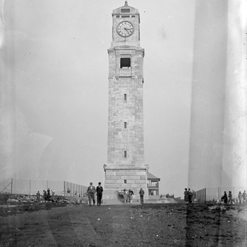 People standing outside of memorial clock tower in park