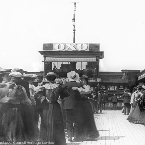 People dancing on the a pier, with advertisement for 'OXO'