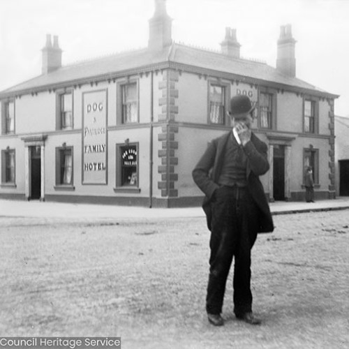 Man standing outside of inn with sign reading 'Dog and Partridge, Family Hotel.'