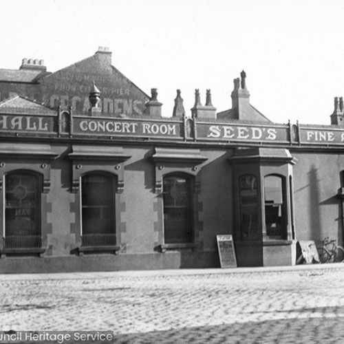 Hotel building viewed from across the street with signs reading 'Foxhall Concert Room, Seeds Fine Ales.'