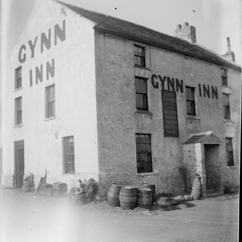 Barrels outside of Inn building with 'Gynn Inn' painted on walls and a sign reading 'James Ashworth, Ale, Porter, Tobacco & Foreign and English Wines.'