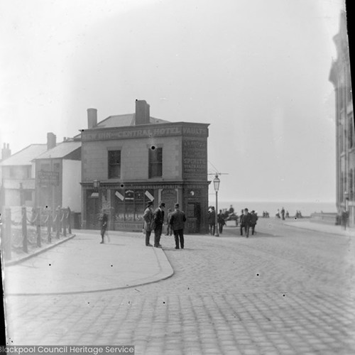 Street scene with inn with sign reading 'New Inn and Central Hotel, Vaults.'