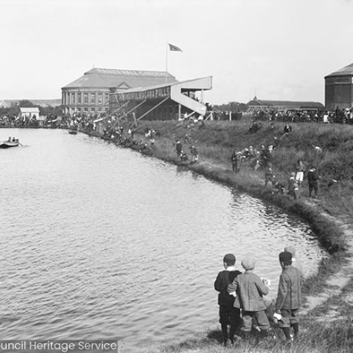 People around lake with grandstand and other buildings