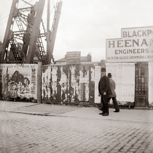 Two men on street outside building site, with a sign reading 'No admittance except on business - Commit no nuisance.'