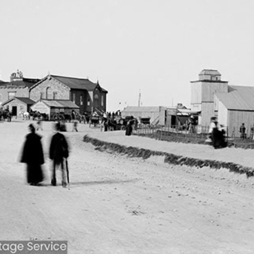 People on cliff tops in front of wooden cabin buildings