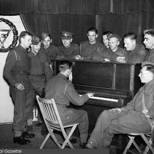 Group of soldiers around a piano, with one playing it.