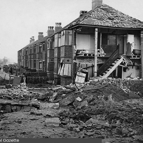 Row of houses, with the end house severely damaged and rubble on the ground.