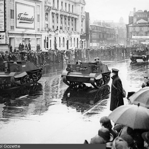 Three Bren Gun Carriers on parade, driving down the Promenade watched by spectators.