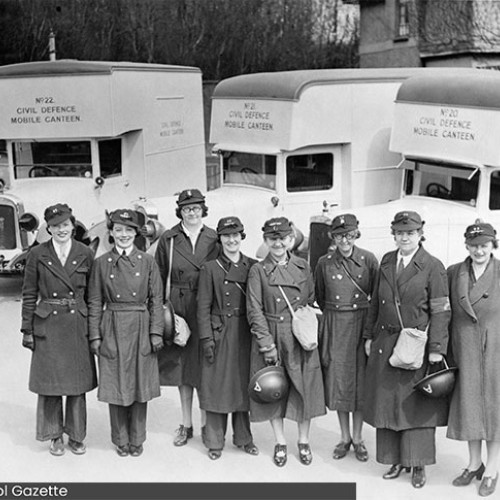 Group of eight women in uniform stood in front of three mobile canteen vehicles.