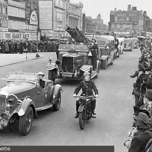 Parade of vehicles, including a fire engine, driving down the Promenade.