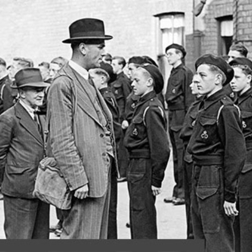 Two men inspecting a group of Civil Defence Messengers, who are stood in line wearing their uniforms.