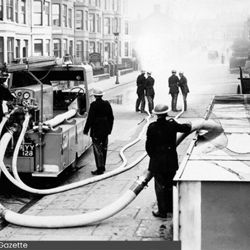 Fire engine getting water from a tank, whilst a group of firemen use the hoses.