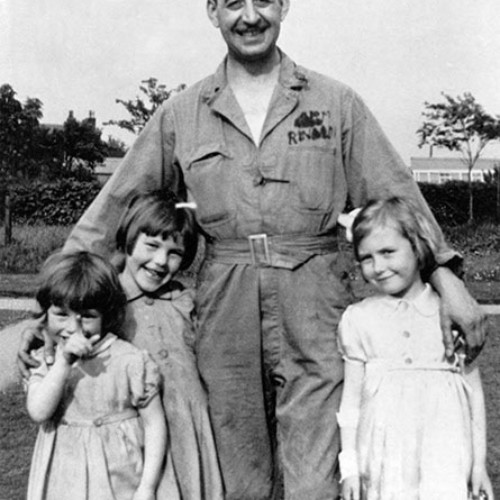 Man wearing a prisoner of war uniform with Renoldi written on it. He is stood with a group of three young girls.