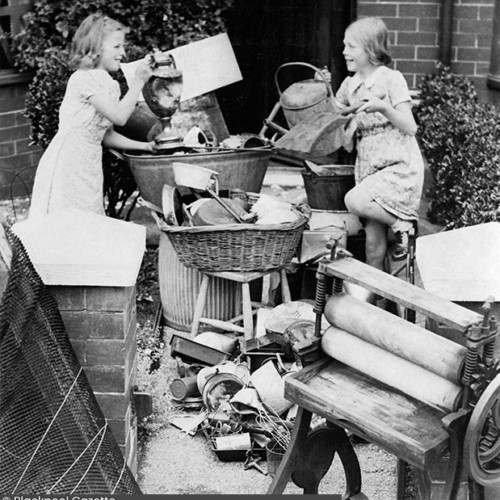 Two girls adding to a pile of mostly metal household items.
