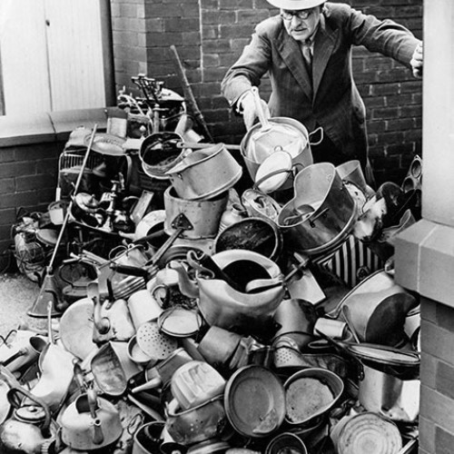 Man adding to a pile of household metal items such as pans and kettles.