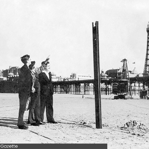 Group of three people inspecting a metal stake which is sticking up on the beach.