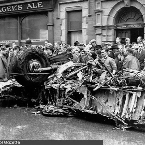 Group of people stood looking at the wreckage of a plane.