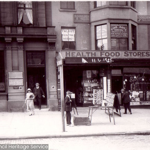 Street scene with a shop frontage and pedestrians walking past.