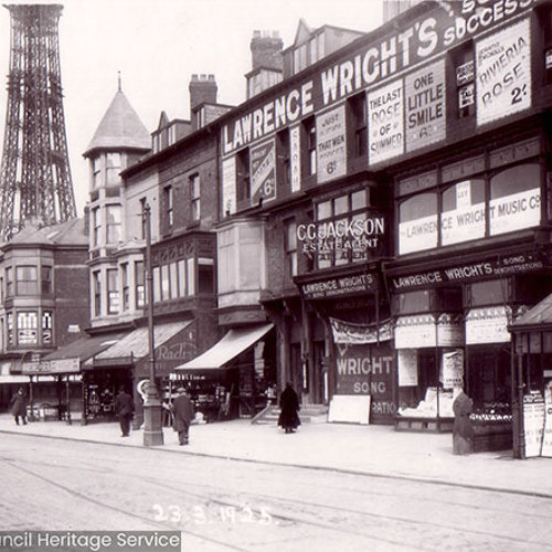 A street scene of a parade of shops with Blackpool Tower in the background.