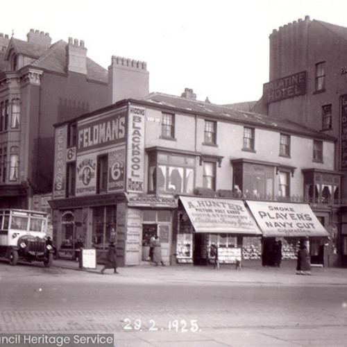 Street scene of shop buildings with two charabanc buses parked outside.