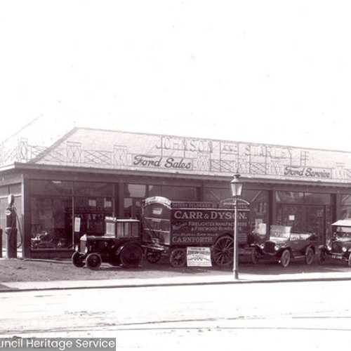 Street scene of a garage building with vintage cars and vans outside.