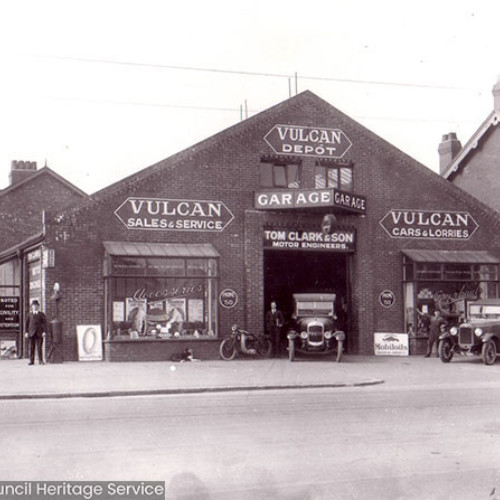 Street scene of a garage building and several vintage cars.