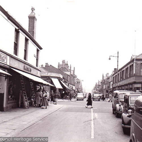 Street scene with pedestrians and traffic outside shops.