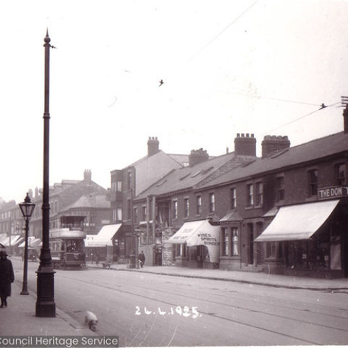 Street scene with a tram moving past shops and houses.