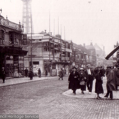 Street scene of pedestrians on busy shopping street with Blackpool Tower in background.