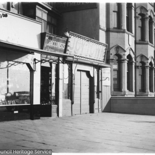 Woman looking through the shop window of a jewellers, which is to the left of a Tobacconists, Joytown and the side of the Palatine Hotel.