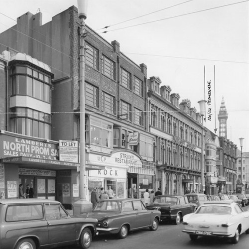 Exterior of a group of buildings, including Lamberts North Prom Sales and the Strand Restaurant.