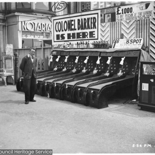 Man stood by arcade machines on the forecourt and sign saying Colonel Barker is Here above.