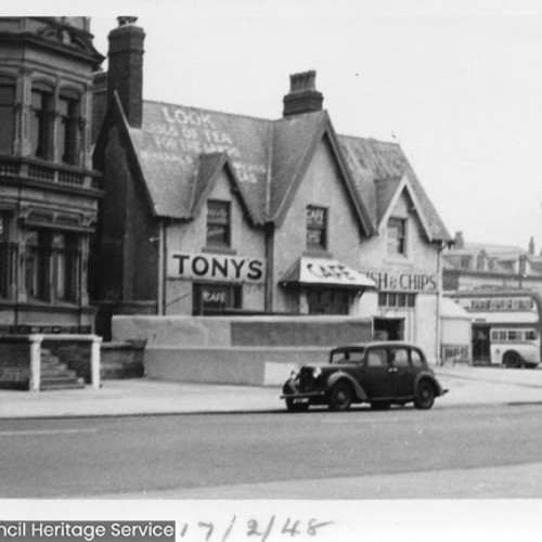 Street corner, with the main building on the corner advertised as Tonys Cafe, selling Fish and Chips.