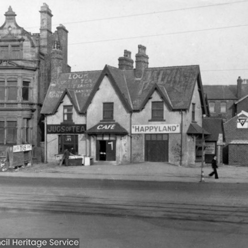 Street corner, with the building on the corner advertising Jugs of Tea, Cafe and Happy Land.