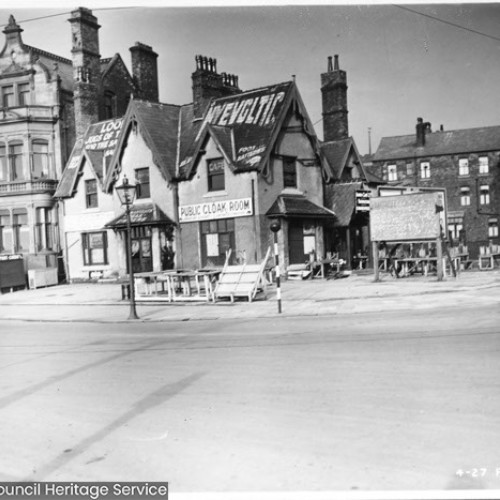 Street corner, with the cafe building on the corner advertising Public Cloak Room.