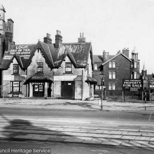 Exterior of a cafe building advertising jugs of tea for the sands.