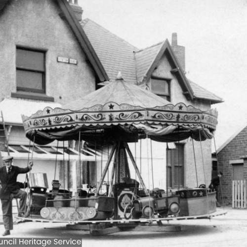 Man leaning on a carousel ride, which has seating in the shape of different forms of transport.