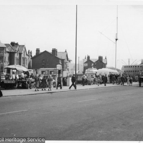 People walking past gift and refreshment stalls lining the street side of the Promenade leading up to the Pleasure Beach.