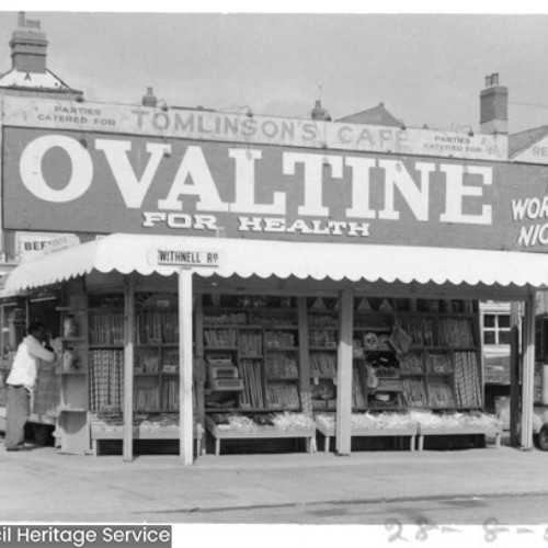 Street corner stall selling rock and a man at the stall window. To the right is the Gypsy Boswell stall and Tomlinson's Cafe is in the background.