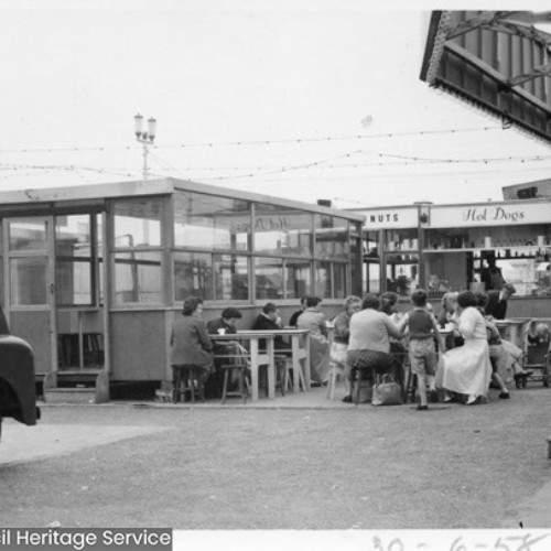 People sat down on chairs outside of a refreshments stall.