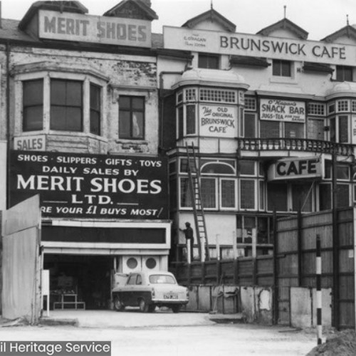 Merit Shoes Ltd which advertises Shoes, Slippers, Gifts and Toys. The Old Original Brunswick Cafe and O'Hagan's Snack Bar, which advertises Jugs Of Tea.