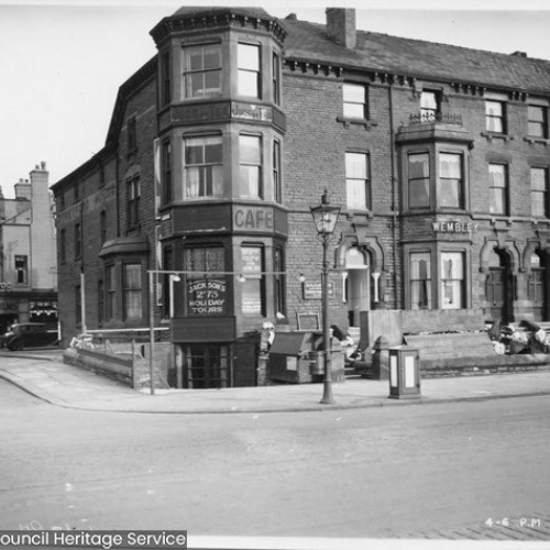 Street corner with the building on the corner advertising Jackson's Holiday Tours and a Cafe with The Wembley next door to the right.