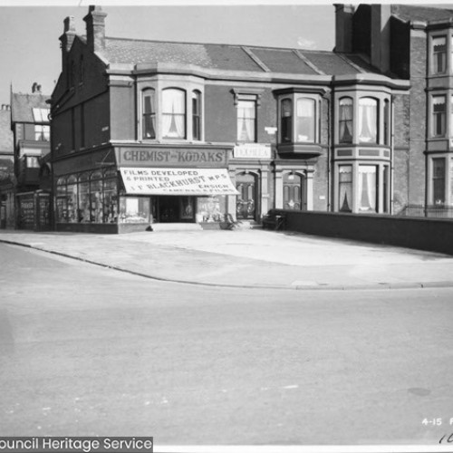 Street corner, with corner building advertised as Chemist and Kodaks.