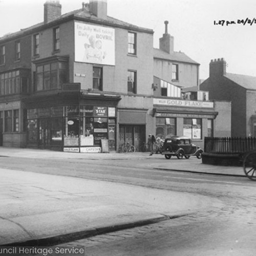 Shops on the street corner, with a large advert for Bovril on the wall above the shop.